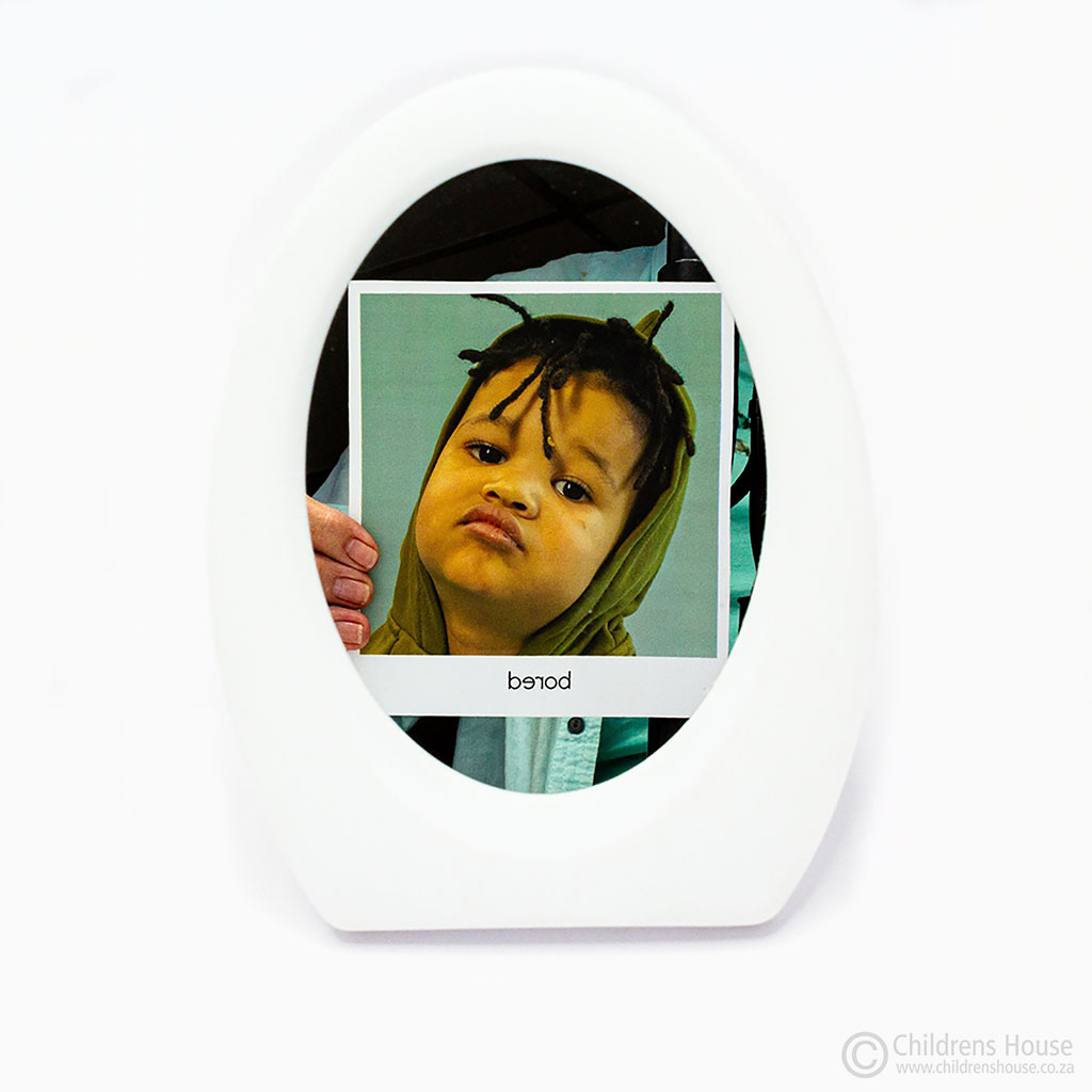 This Featured image displays a small, plastic, white framed mirror. The mirror is reflecting on of the Facial Expression cards, an activity sold by Childrens House.