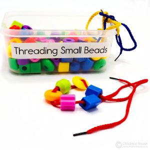 This Featured image displays a box of small, plastic shapes and laces. The threading small beads activity is sold by Childrens House.
