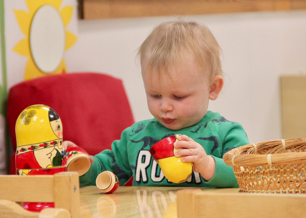 Farmington Valley Academy Montessori - Toddler Assistant, hero image of a toddler at work. The toddler is opening and closing a Russian Matryoshka nesting doll. He has showing great focus and concentration.