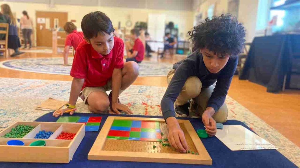 Butler Montessori - AMI LE Guide. The picture shows a lower elementary class at work. 2 Boys, busy with a Mathematics activity. At this age, students start asking questions and exploring ideas such as: How did the world begin? When did humans develop? How does this machine work? This is why the foundation for all courses of study is the “Great Lessons.” These lessons provide the “big picture” of language, mathematics, astronomy, earth science, geography, chemistry, physics, biology, history, anthropology, social studies, music, and art.
