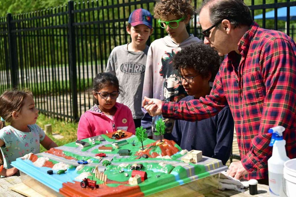 Butler Montessori - AMI LE Guide. The image shows a language class working with the Montessori Farm Grammar activity. Our teachers are Association Montessori Internationale (AMI) certified, which means they've undergone rigorous training to ensure they can best guide your child's natural development. This AMI recognition signifies our dedication to Dr. Montessori's methods, including mixed-age classrooms, high-quality materials, and a philosophy that fosters independence, curiosity, and a love of learning.