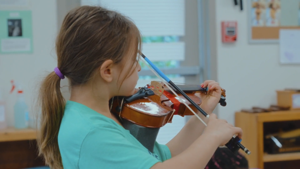 Montessori School of Raleigh Lead LE Guide. A lower elementary student playing the violin during Music class.