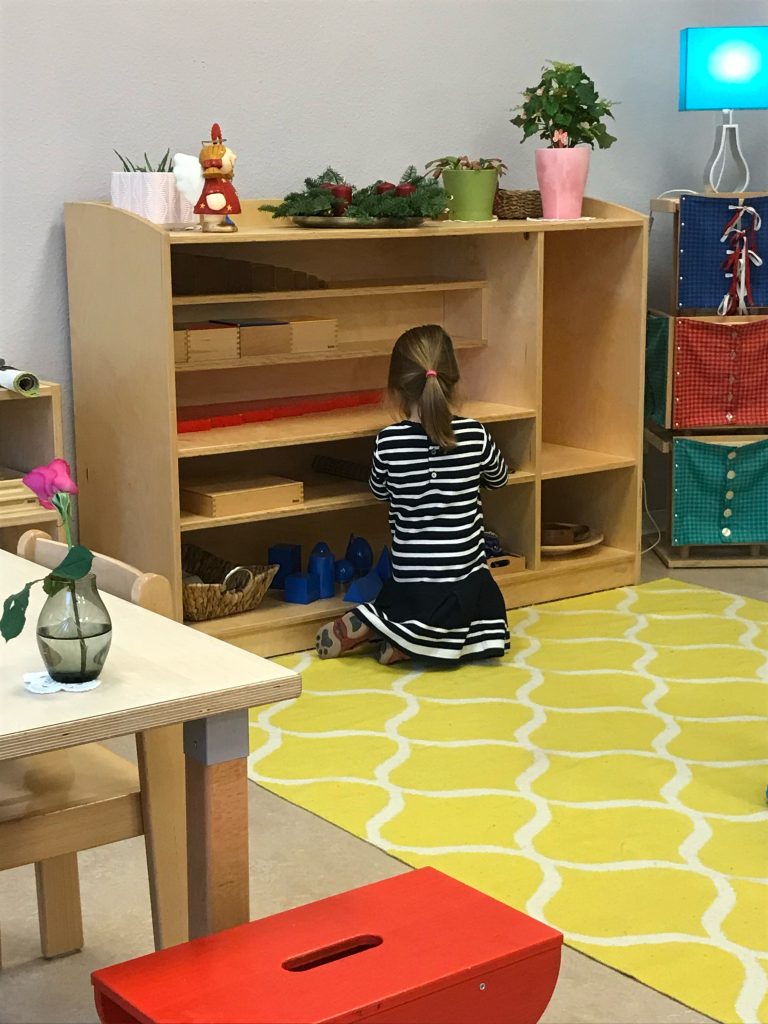 A Child kneeling at a low shelf, choosing a material in a Montessori Environment